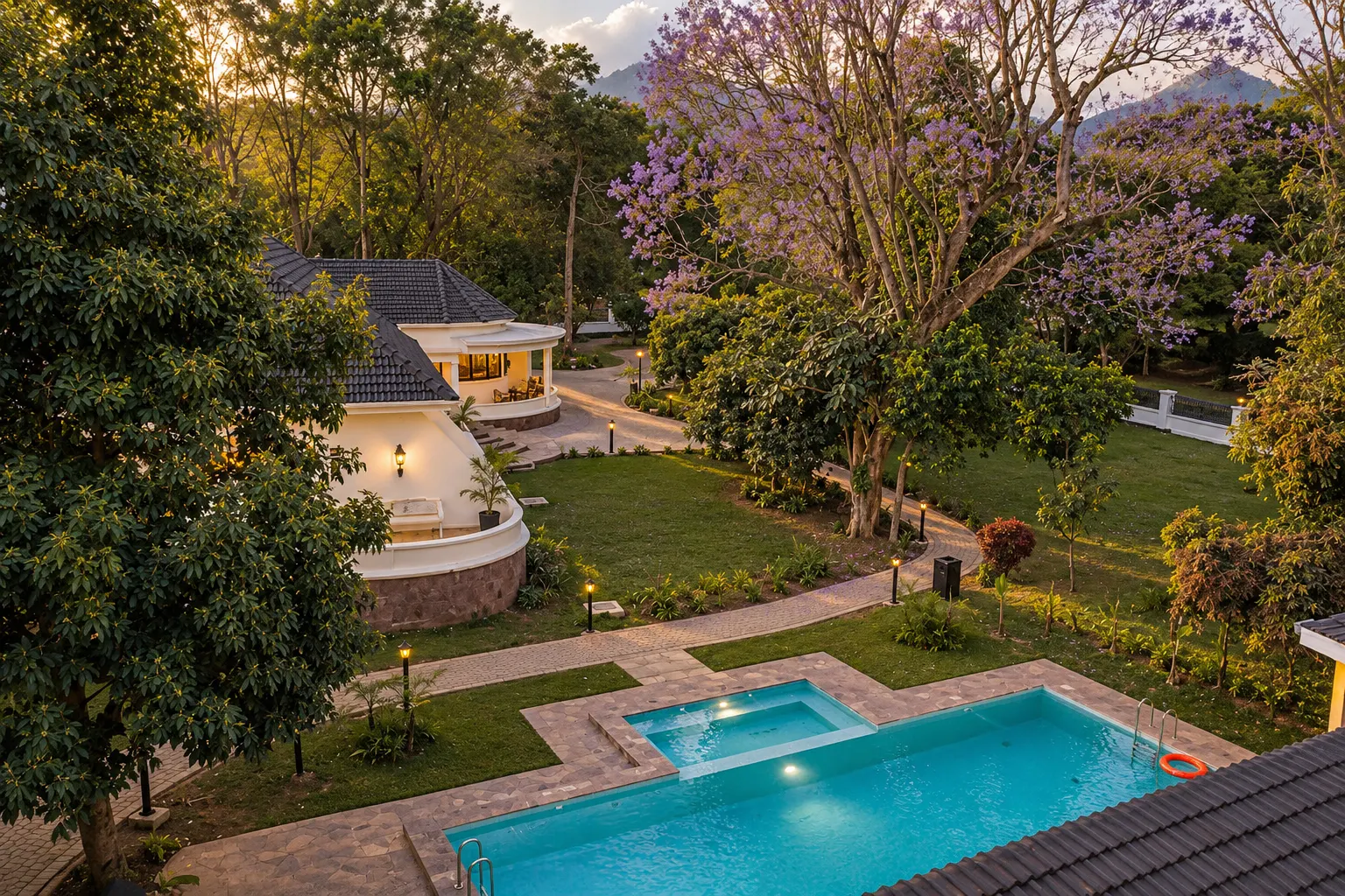 Haile Boutique Hotel at golden hour — a white 1950s house with a wraparound veranda and a tiled roof, palms and a warm brick forecourt.