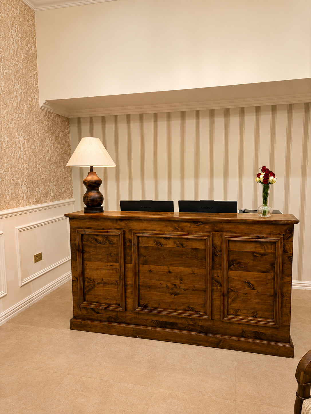 The reception desk, in walnut, with a shaded lamp and cut roses.